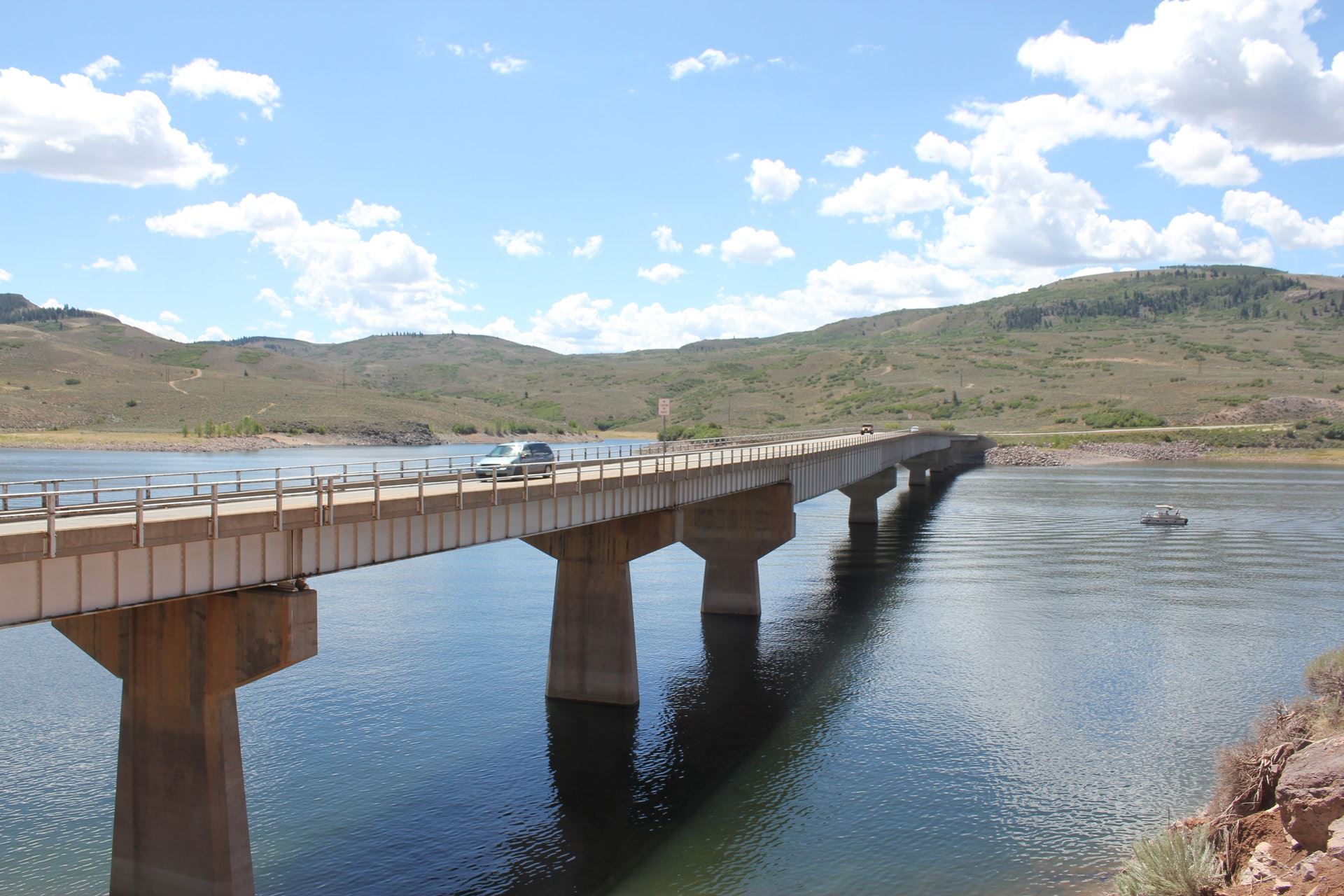 Lake Fork Bridge on a sunny day with cars crossing and a boat on the lake heading to the left. 