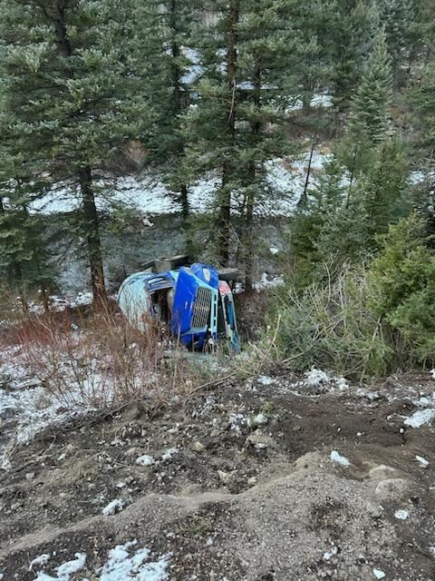 Propane transport truck on its side off a road in front of trees
